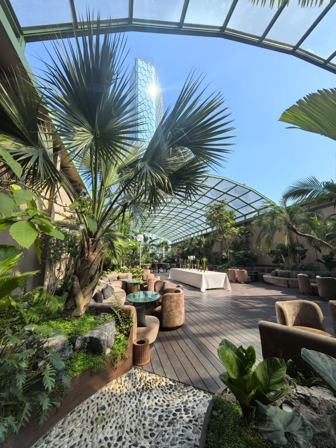 Garden terrace beneath a glazed sunroom roof with palms and outdoor seating
